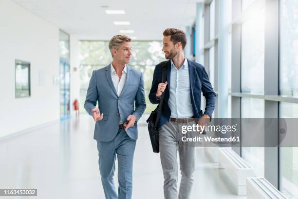 two businessmen walking and talking in a passageway - business man walking fotografías e imágenes de stock