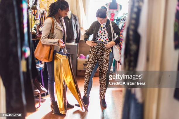 two young women looking at clothes in a vintage clothes shop - essayer photos et images de collection