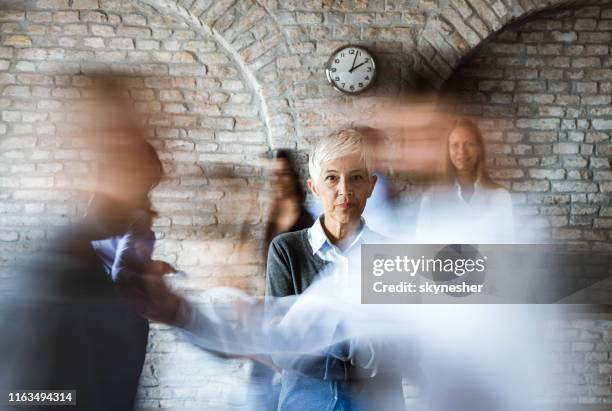 senior businesswoman with crossed arms among people in blurred motion. - large group of people serious stock pictures, royalty-free photos & images