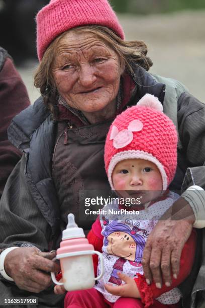 Elderly Ladakhi woman holds her grandchild as she watches Buddhist monks perform ancient sacred dances during the Lamayuru Masked Dance Festival in...