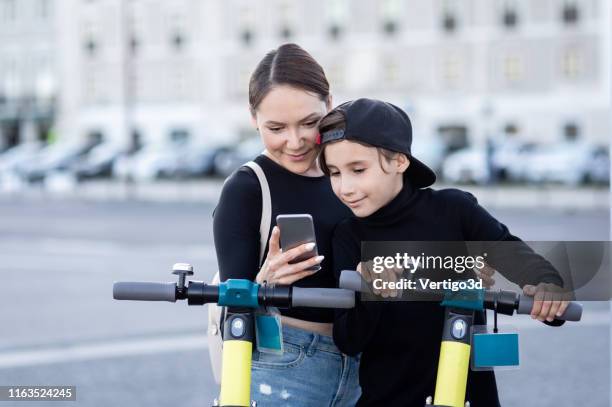 moeder en zoon met behulp van een mobiele telefoon voor het ontgrendelen van een elektrische scooter door app - 3 teenagers mobile outdoors stockfoto's en -beelden