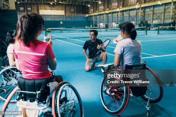 young female wheelchair tennis player listening to her coach at an indoor tennis court - wheelchair tennis stockfoto's en -beelden