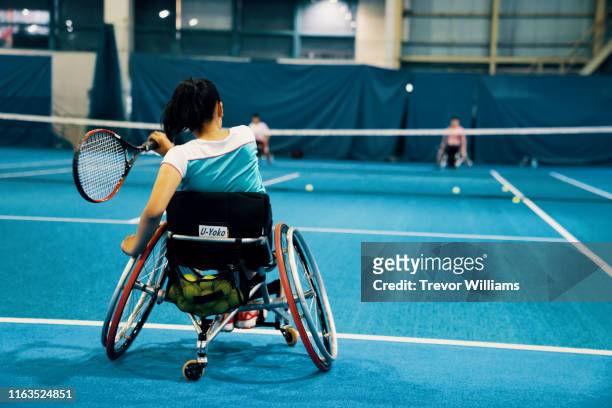 teenage girls playing and practicing wheelchair tennis together at an indoor tennis court - adaptive athlete - fotografias e filmes do acervo