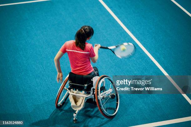 high angle view of a teenage girl playing and practicing wheelchair tennis at an indoor tennis court - wheelchair tennis stock pictures, royalty-free photos & images