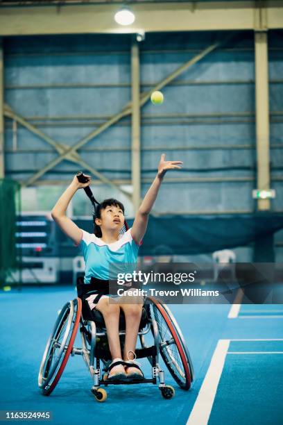 teenage girl playing a wheelchair tennis match at an indoor tennis court - wheelchair tennis stock pictures, royalty-free photos & images