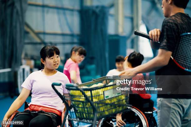 Young female wheelchair tennis players practice together with their coach at an indoor tennis court