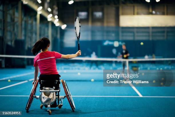 teenage girl practicing wheelchair tennis together with her coach at an indoor tennis court - wheelchair tennis stockfoto's en -beelden
