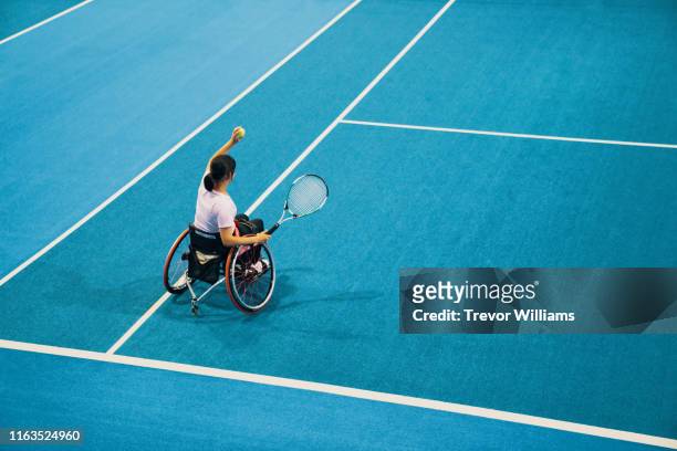 high angle view of a teenage girl playing and practicing wheelchair tennis at an indoor tennis court - match sport stock-fotos und bilder