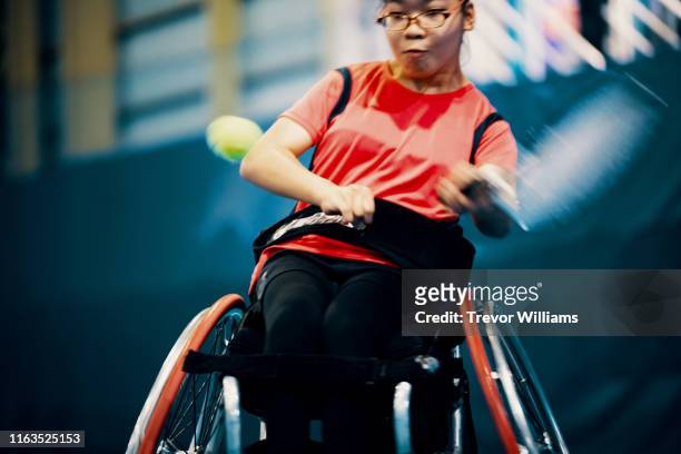Teenage girl playing and practicing wheelchair tennis at an indoor tennis court