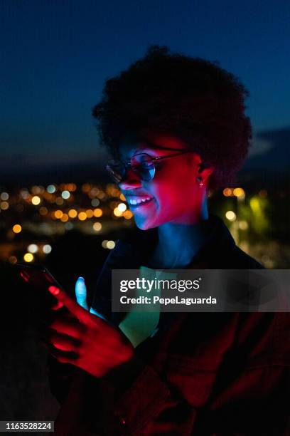 young woman using her mobile phone at night with the city at background - mobile technology imagens e fotografias de stock