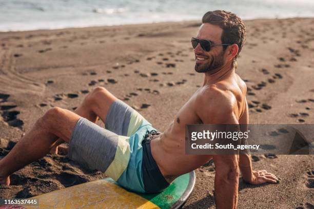 surfer relaxing on the beach alone - hunky guy on beach stock pictures, royalty-free photos & images