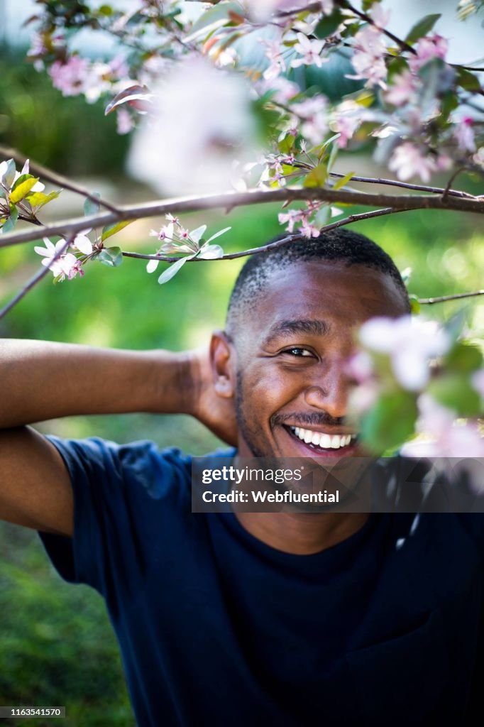 Young black man standing outdoors behind tree branches