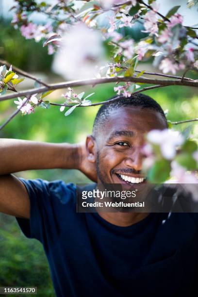 Young black man standing outdoors behind tree branches