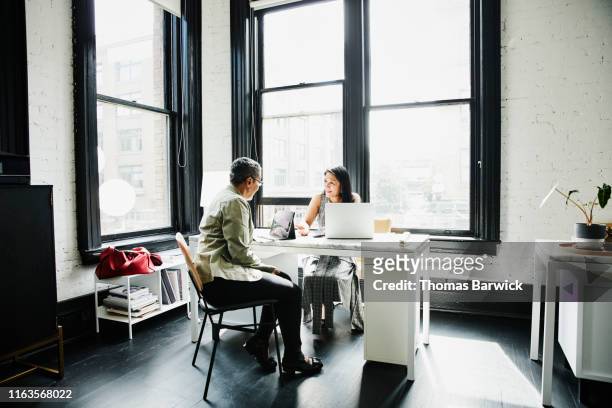 Smiling mature female business owner in discussion with financial advisor at desk in office