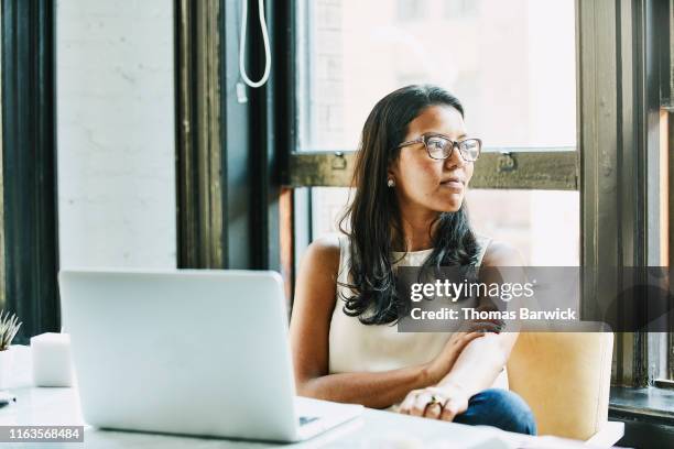 businesswoman looking out window while seated at desk in office - smart windows stock-fotos und bilder