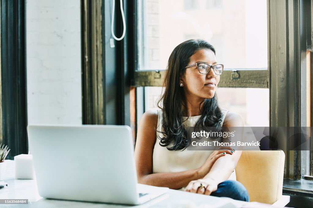 Businesswoman looking out window while seated at desk in office