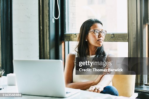 Businesswoman looking out window while seated at desk in office Businesswoman looking out window while seated at desk in office