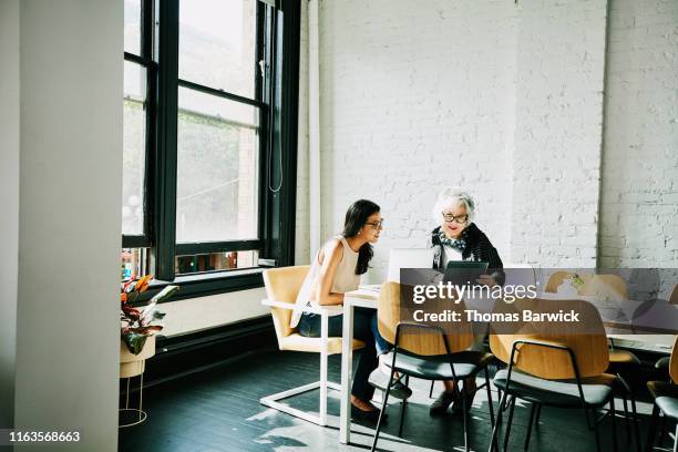 senior businesswoman presenting project on digital tablet to colleague in conference room - féminin modèle photos et images de collection