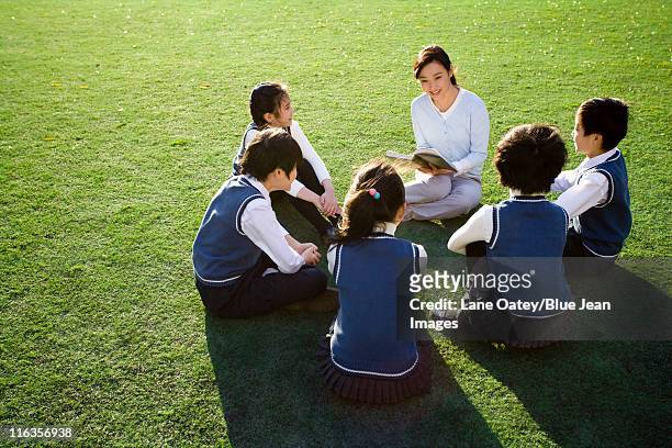 teacher reading to students on grassy field - bambini seduti in cerchio foto e immagini stock