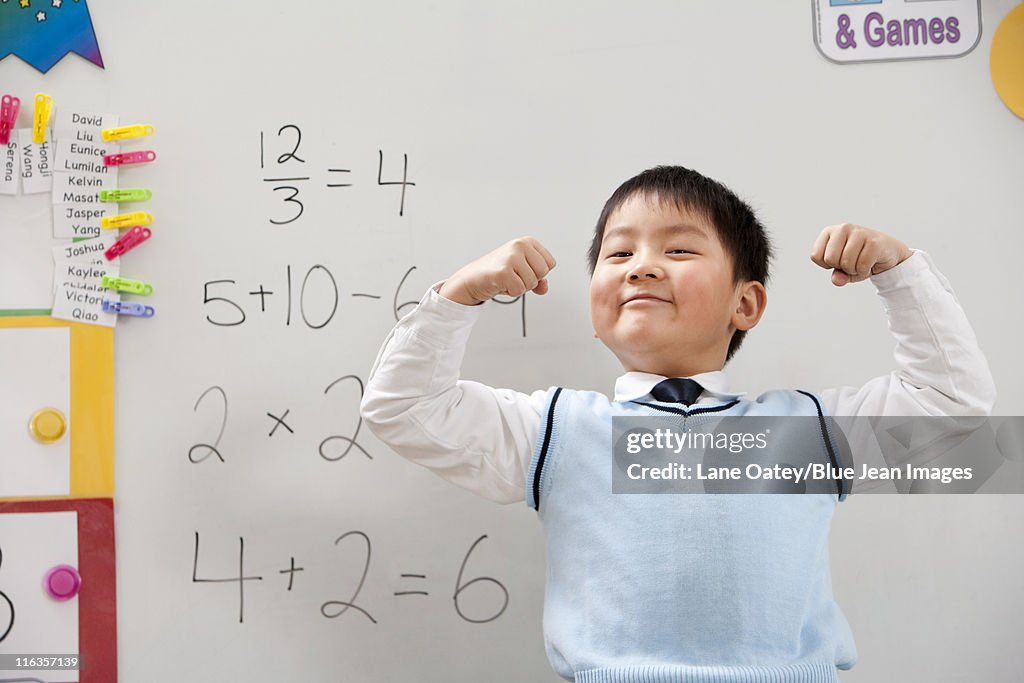 A young student flexing his muscles in front of a whiteboard