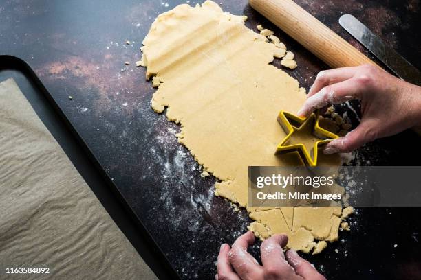 high angle close up of person cutting out star-shaped cookies from cookie dough. - pastry cutter stockfoto's en -beelden