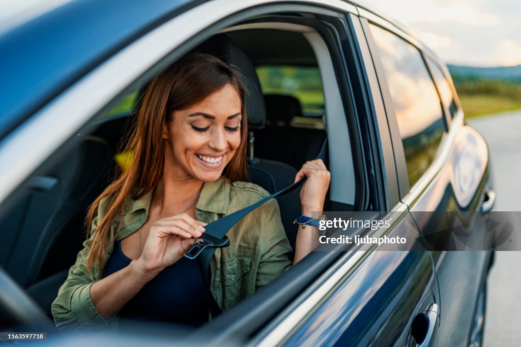 Photo of a business woman sitting in a car putting on her seat belt