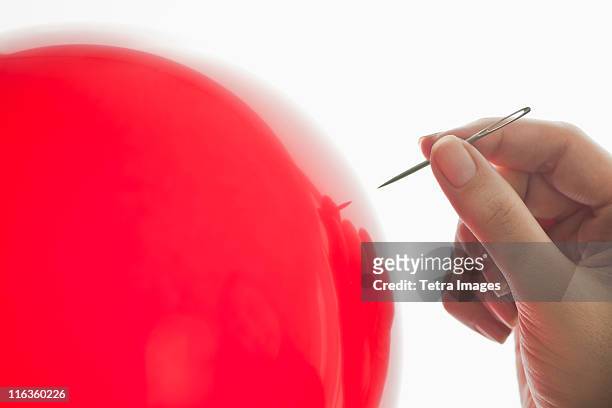 studio shot of woman holding needle close to red balloon - blowing up balloon stock-fotos und bilder