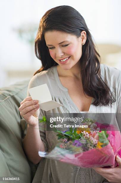 usa, new jersey, jersey city, young woman holding bouquet and reading greeting card - receiving card stock pictures, royalty-free photos & images