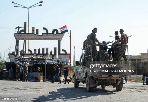 Members of the Syrian government forces sit atop a military vehicle in front of a welcome sign in the strategic town of Khan Sheikhun on August 24...