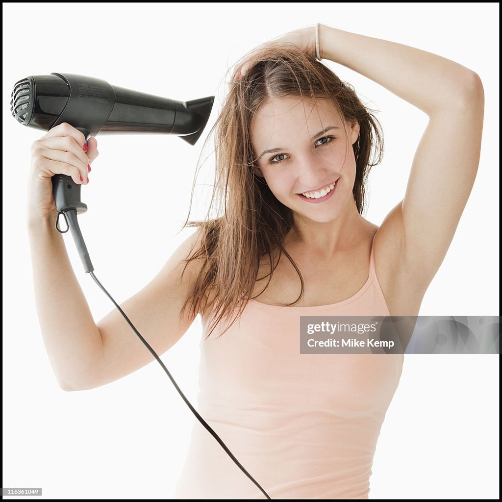 Studio portrait of young woman blow drying hair