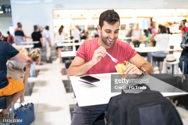 mann isst in flughafen food court während des wartens auf flug - food court stock-fotos und bilder