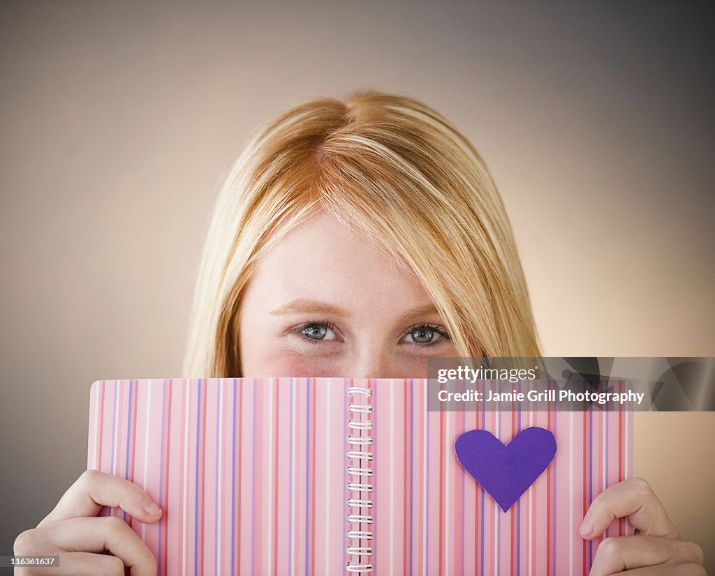 Young woman hiding behind diary