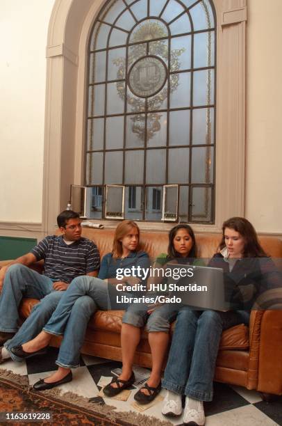 Group of students sit on a couch and study using an Apple Computer laptop under an ornate window on the Homewood Campus of the Johns Hopkins...