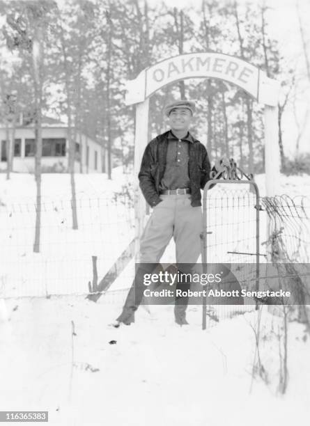 Portrait of future newspaper publisher John H. Sengstacke as he poses in the snow at the entrance gate to the Oakmere Hotel, Idlewild, Michigan,...