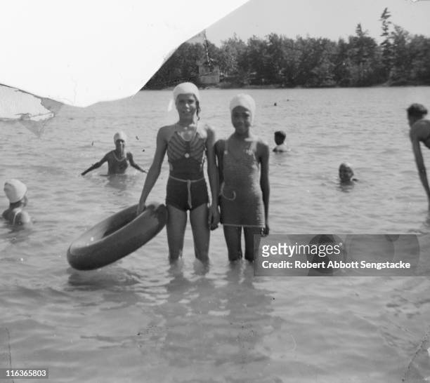 Portrait of a pair of unidentified young woman , one with an inflatable tube in her hand, as they pose in the water of Idlewild Lake, Idlewild,...