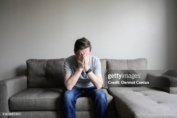 depressed mature man sitting on couch - manos a la cabeza fotografías e imágenes de stock