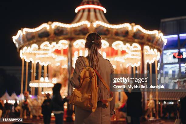 young woman by carousel at night - karusell stock-fotos und bilder