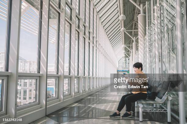an asian chinese female tourist at the airport sitting and using her digital tablet surfing the net - munich airport stock pictures, royalty-free photos & images