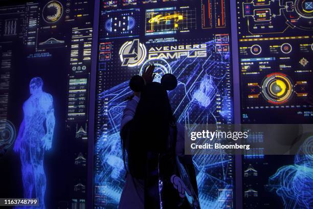 An attendee wearing Mickey Mouse ears uses an interactive wall display at the Marvel Studios Avengers Campus preview during the D23 Expo 2019 in...