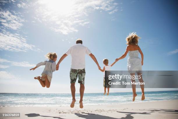 family holding hands and jumping on beach - jumping sun stock pictures, royalty-free photos & images