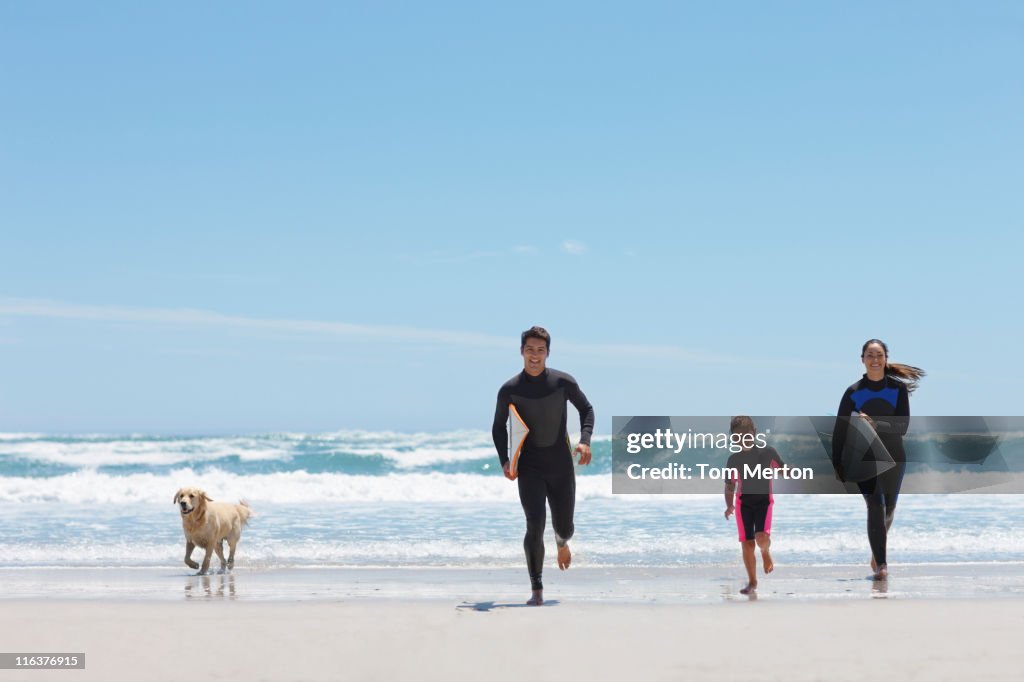 Family with surfboards running on beach