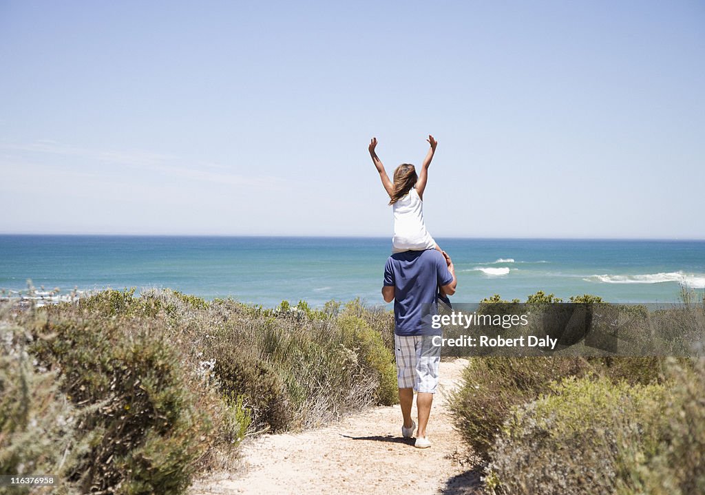 Father carrying daughter on shoulders on beach path