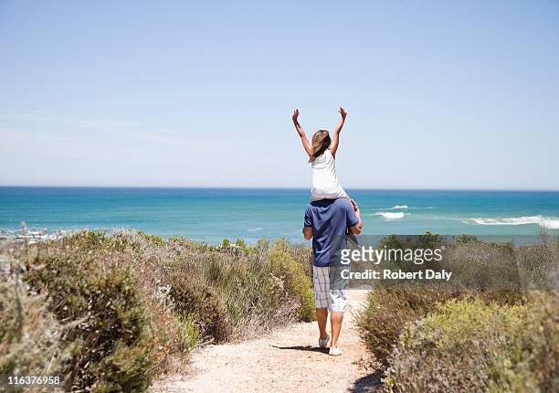father carrying daughter on shoulders on beach path - carrying on shoulders stock pictures, royalty-free photos & images