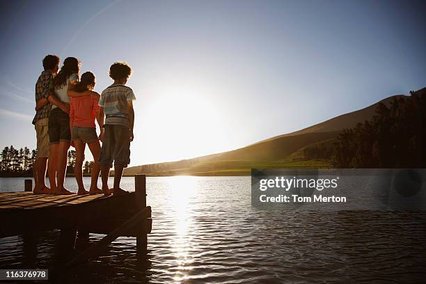 familie bei sonnenuntergang am dock am see - sun flare couple stock-fotos und bilder