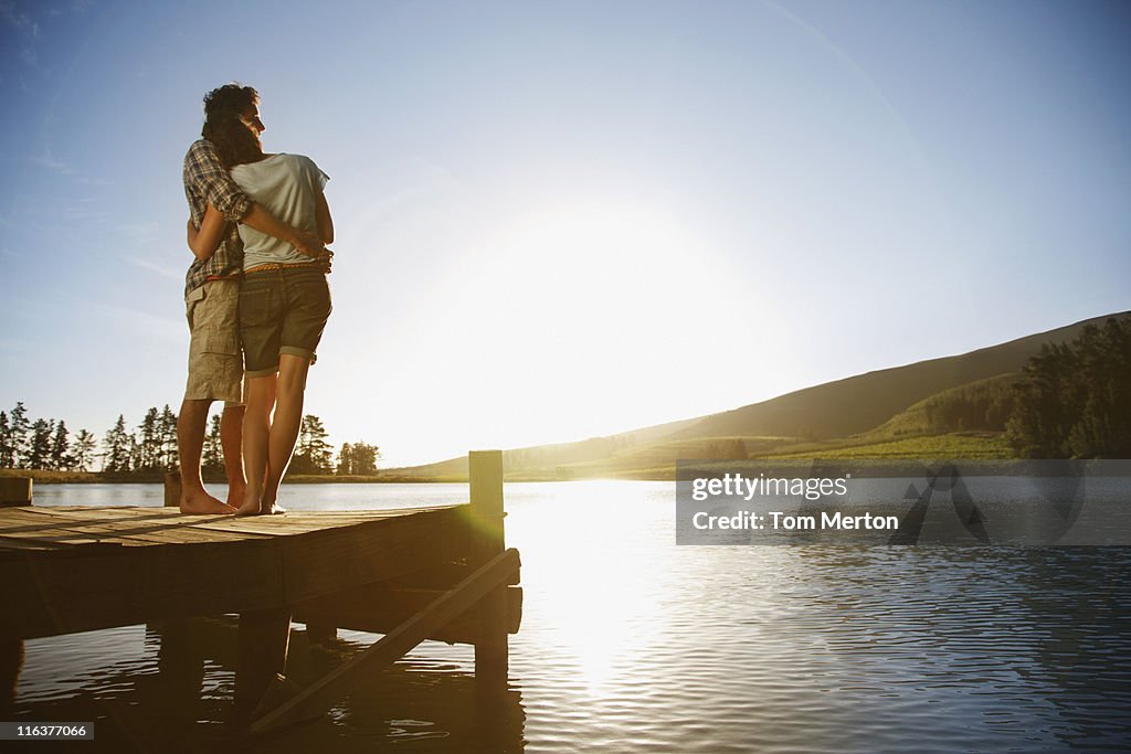 Couple on dock hugging and watching sun set over lake