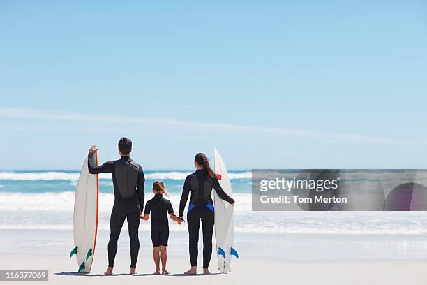 family in wetsuits with surfboards holding hands on beach - surfer wetsuit stockfoto's en -beelden