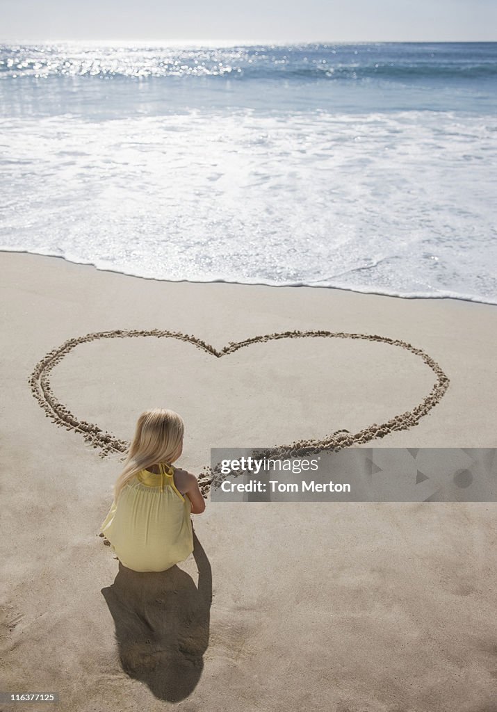Girl drawing heart in sand on beach
