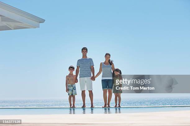 family standing at edge of infinity pool with ocean in background - infinity pool stockfoto's en -beelden