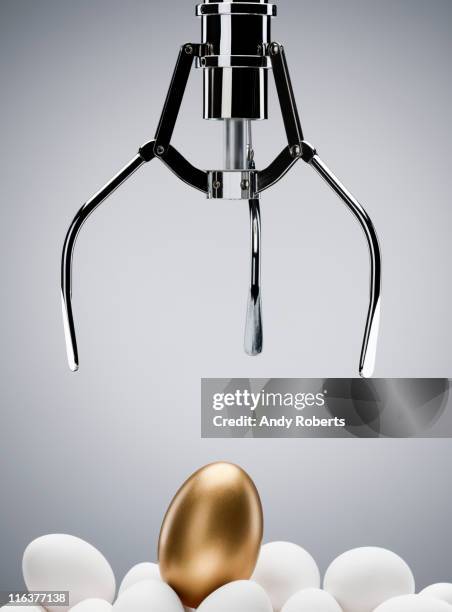 mechanical claw reaching for golden egg - mechanical claw stock-fotos und bilder