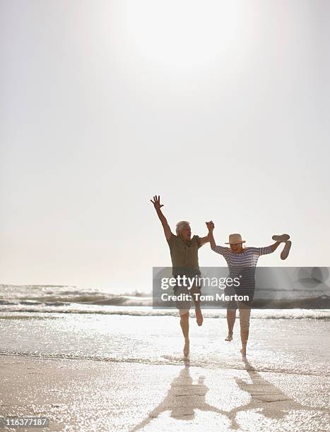 altes paar springen am strand - mann freudensprung sonne vorderansicht leger stock-fotos und bilder